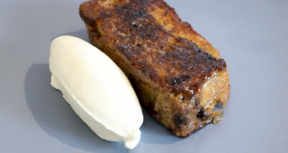An image of a pan fried panettone pudding, with golden brown slices of the dessert arranged on a plate. The pudding has a creamy, layered appearance, with bits of chopped fruit visible.