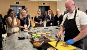 Freshly prepared chef demonstrates cooking techniques to engaged business audience at BM Caterers event.