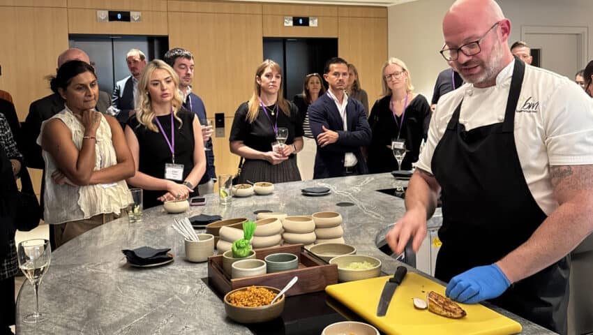 Freshly prepared chef demonstrates cooking techniques to engaged business audience at BM Caterers event.